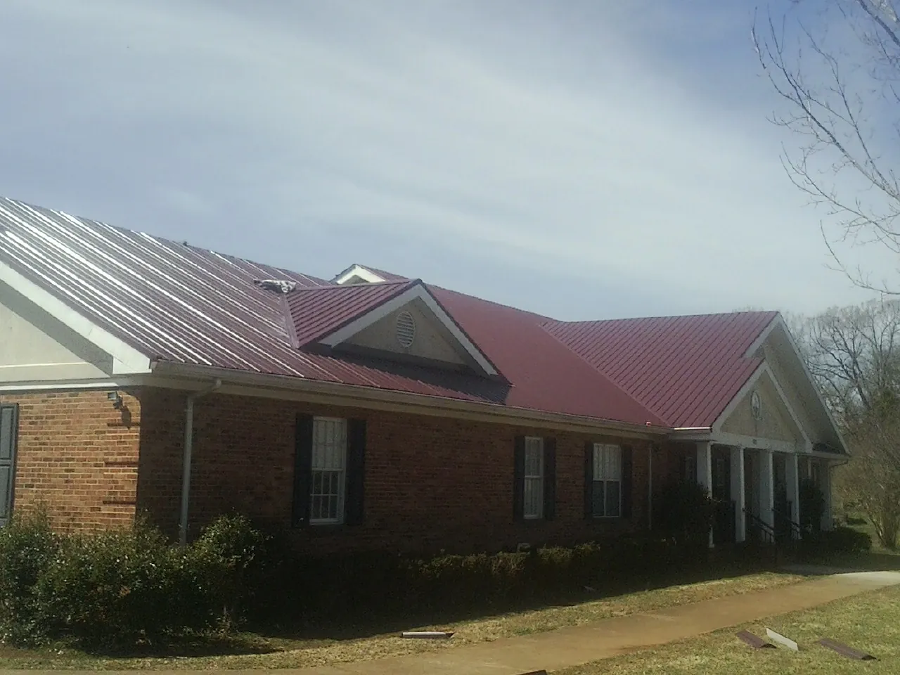 Red metal roof with gabled entries on a long brick building, from a Hail Damage Roof Repair job in Duck River