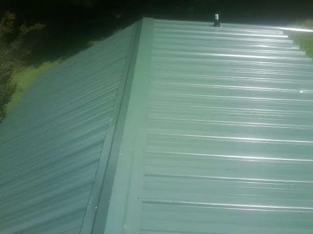 New green metal panels meeting at the ridge of a roof — Flat Roof Repair work by our crew in Duck River