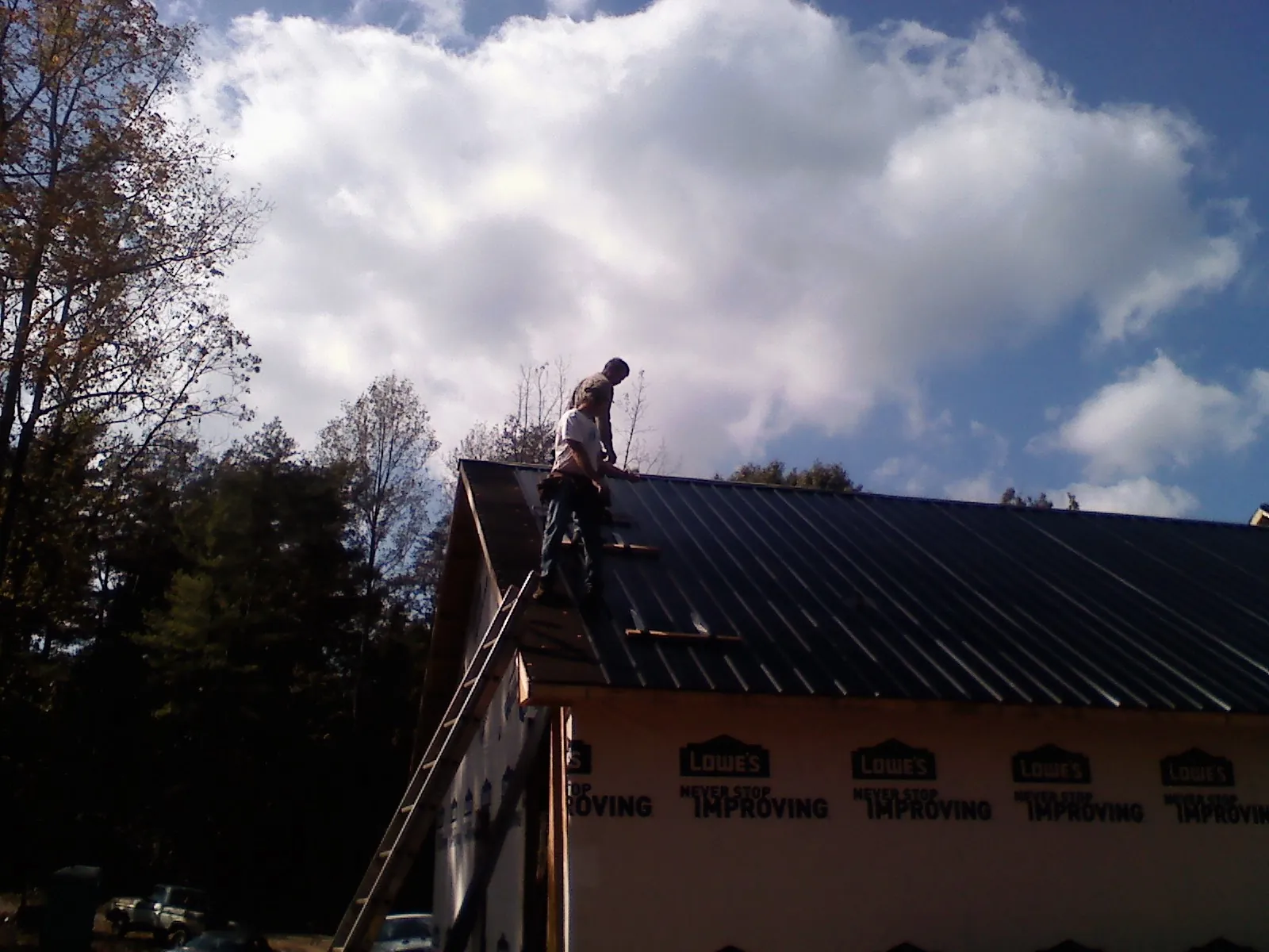 Roofer fastening dark metal panels high against a cloudy sky, from a Roof Inspection job in Duck River