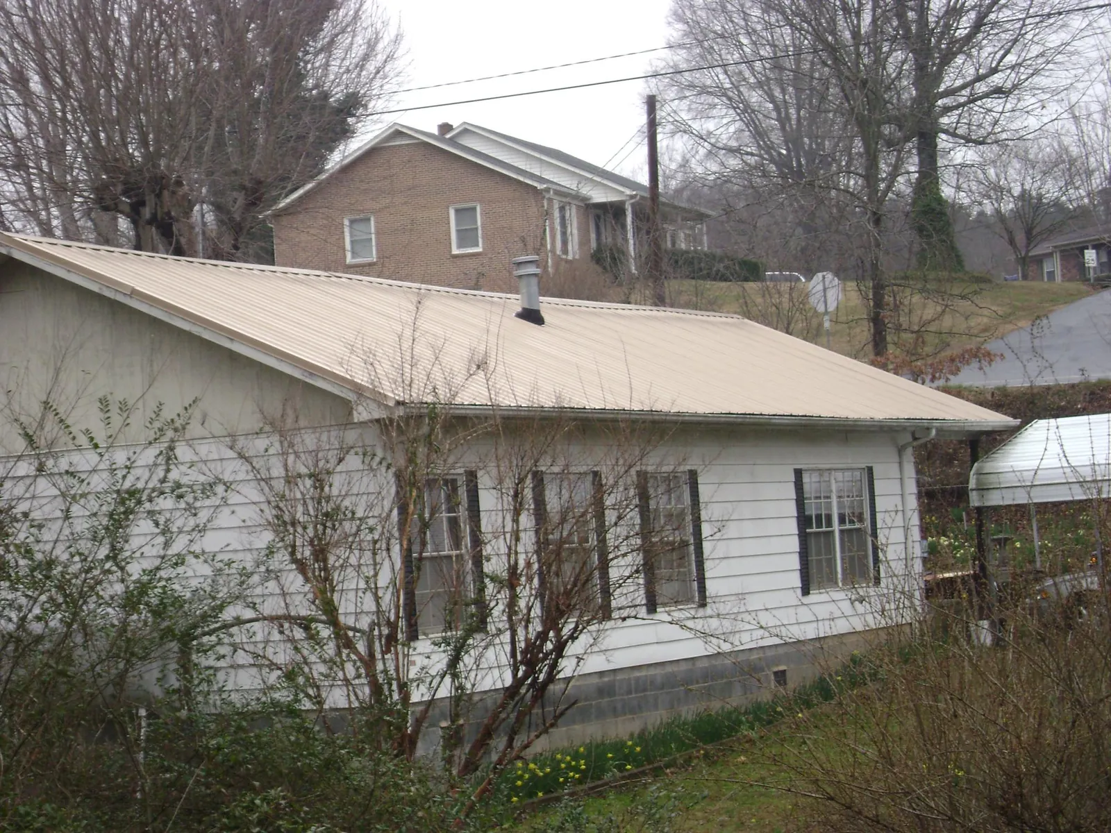 Tan metal roof on a white sided house set into a hillside — Commercial Roofing by Roofing Brothers in Duck River