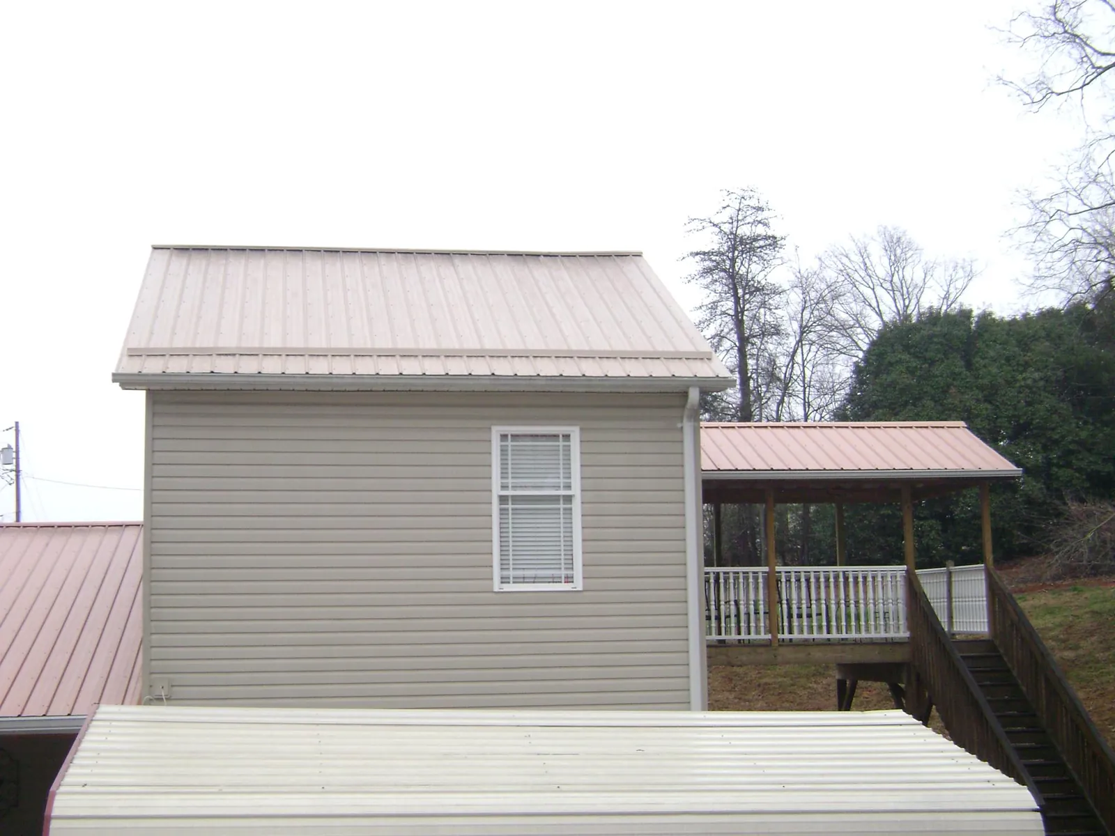 Tan metal roofs on a two story addition and attached porch, from a Roof Replacement job in Duck River